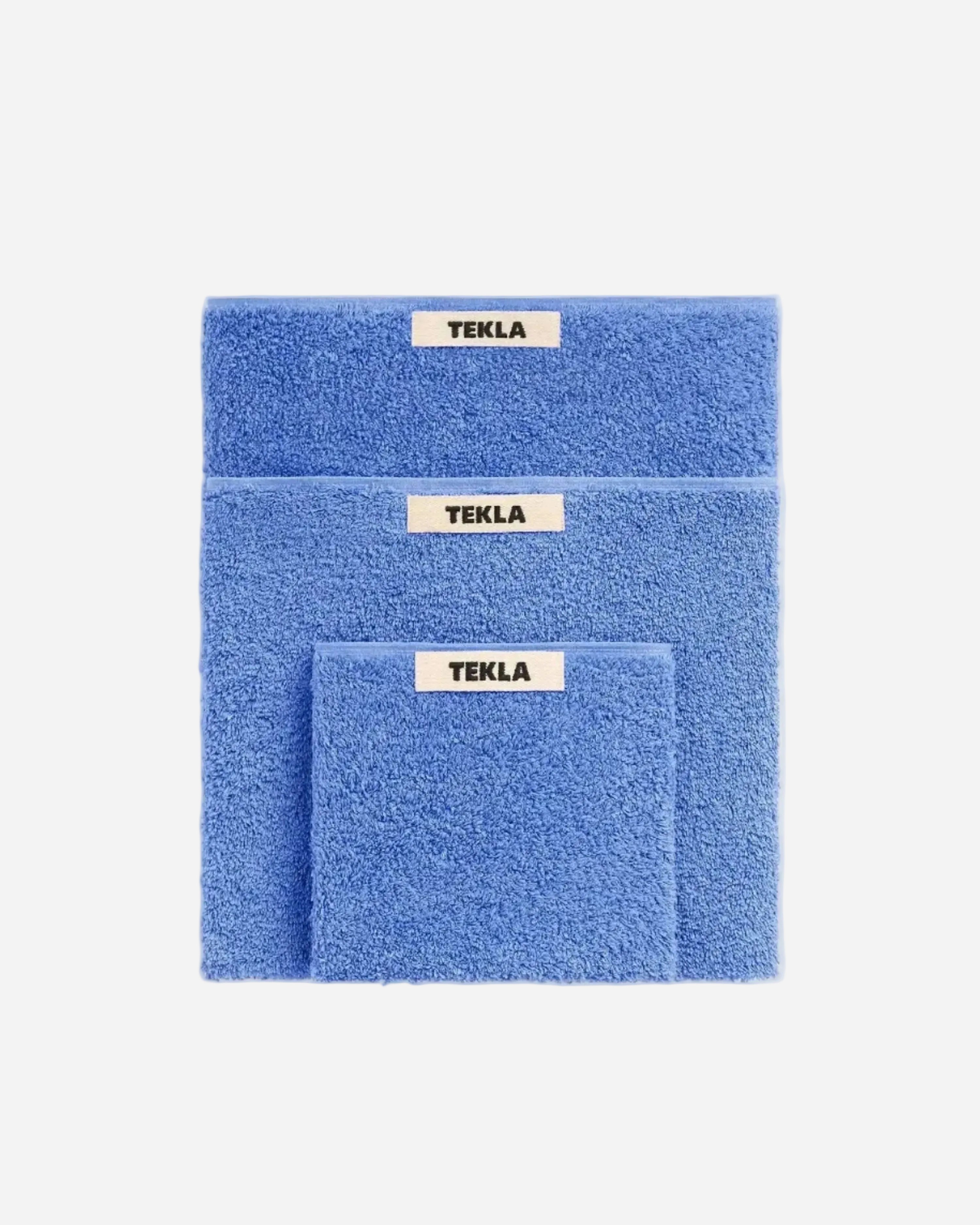 Set of blue towels with 'TEKLA' labels on a white background